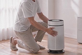 A person using both hands to touch or adjust the textured outer cover of an white cylindrical air purifier.